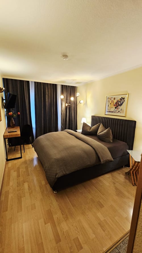 Modernes Hotelzimmer im Soho Hotel Düsseldorf mit schwarzem Bett, gelben Wänden, dunklen Vorhängen und Holzparkett
