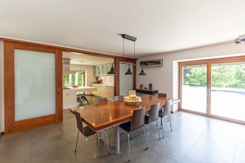 Sala de jantar moderna com mesa de madeira, cozinha e portas de vidro deslizantes que abrem para o terraço da piscina na vila Quinta Trindade