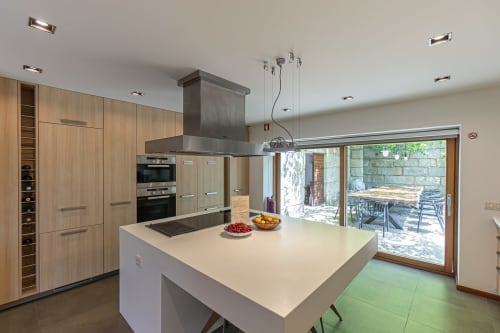 Cozinha moderna com ilha, armários em madeira e portas de vidro que se abrem para o terraço da villa Quinta Trindade em Arouca