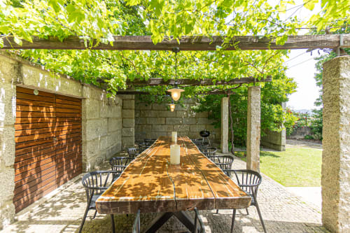Área de refeições ao ar livre sombreada da quinta Trindade em Arouca com mesa de madeira, cadeiras pretas e pérgola coberta de videiras