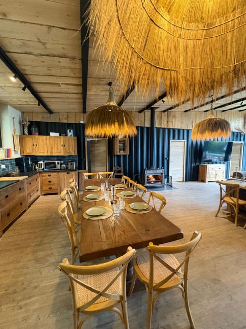 Salle à manger chaleureuse avec table en bois, lampes suspendues tressées et cheminée au Village Du Moulin à Sizun, France
