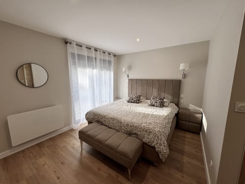 Chambre moderne du gîte Chez Babeth au Village Du Moulin, Sizun, avec lit queen-size, tête de lit grise, banquette et vue sur le jardin