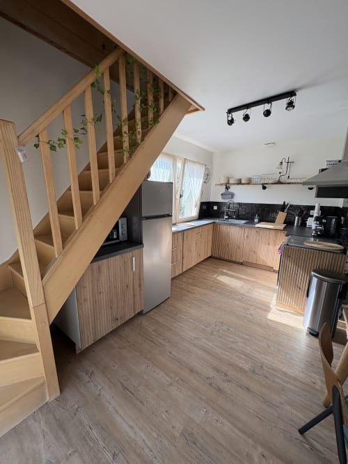 Cuisine moderne avec escalier en bois, appareils en acier inoxydable et dosseret noir au gîte Kerroc'h, Sizun