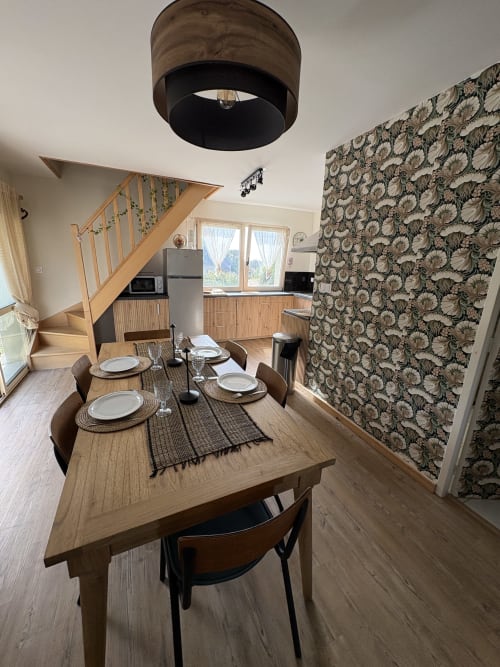 Salle à manger du gîte Kerroc'h au Village Du Moulin, Sizun, avec table en bois, chaises modernes et papier peint floral