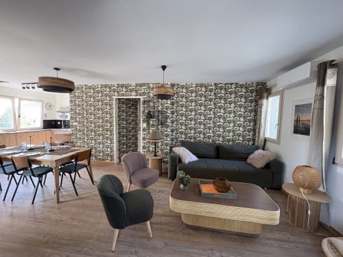 Salon moderne du gîte Le Village Du Moulin à Sizun avec canapé noir, coin repas, meubles en bois et motifs variés
