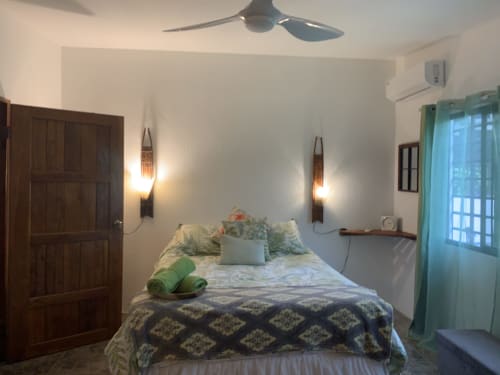 Cozy bedroom at El Litoral Panama with queen bed, ceiling fan, AC unit, wall sconces, and garden view through glass door
