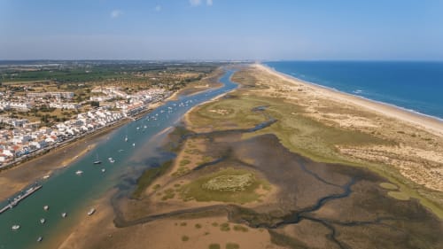 Vista aérea da paisagem costeira de Tavira com estuário, praia e edifícios brancos à beira-mar