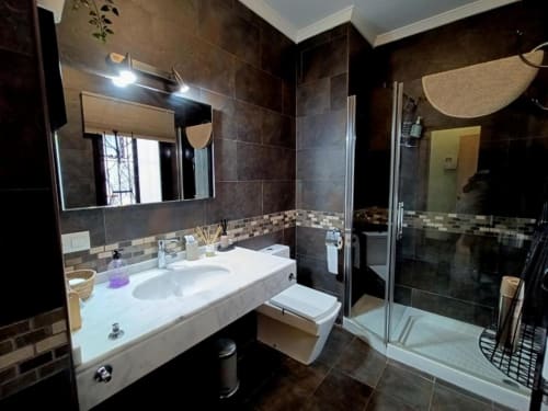 Baño moderno del apartamento Top Home Évora, Jerez de la Frontera, con paredes de azulejos oscuros, lavabo blanco, espejo, inodoro y