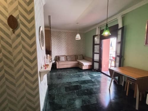 Moderno salón en Jerez con paredes verdes, papel pintado chevron beige, sofá, mesa de comedor y vistas a la ciudad a través de