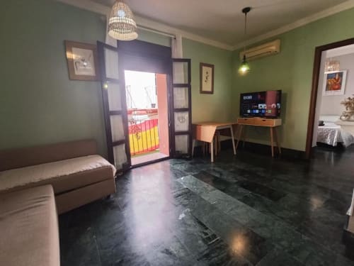 Sala moderna con paredes verdes, sofá, escritorio con TV y puerta al balcón en Jerez de la Frontera