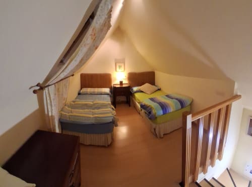 Acogedora habitación en buhardilla de la cabaña invernal Sierra Nevada con dos camas, muebles de madera, iluminación cálida y vistas a las montañas
