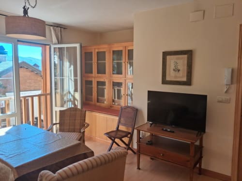Sala de estar con vistas a la montaña en Casa Buenavista, cabaña invernal en Sierra Nevada, Granada, con televisor, muebles de madera y balcón
