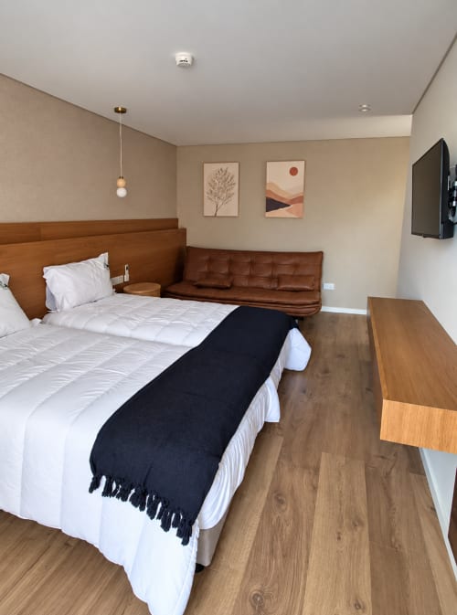 Quarto moderno no House Park em Esposende com cama de madeira, sofá marrom, roupa de cama branca e TV na parede