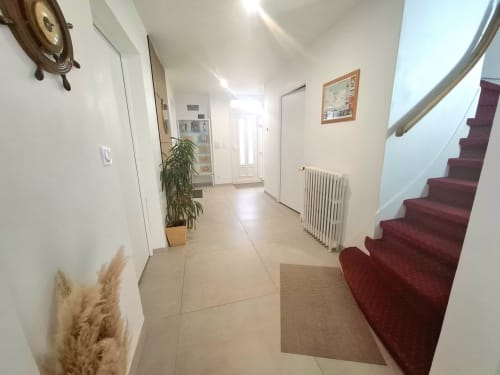 Couloir lumineux de La villa Cassinne B&B à Montebourg avec carrelage beige, escalier à tapis rouge, murs blancs et plantes en pot