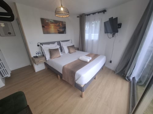 Chambre moderne à La villa Cassinne avec lit king-size, linge blanc, TV, luminaire suspendu et vue sur le jardin à Montebourg