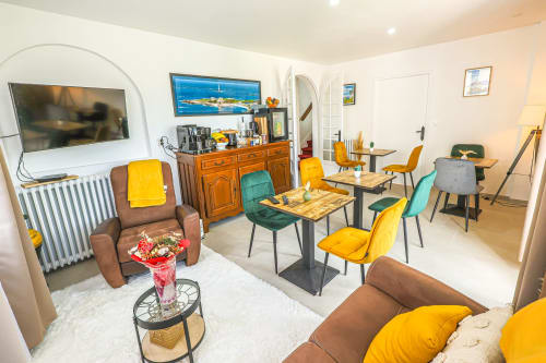 Chambre moderne et accessible à La villa Cassinne avec sièges jaunes et bleus, tables de salle à manger et télévision écran plat à Montebourg.