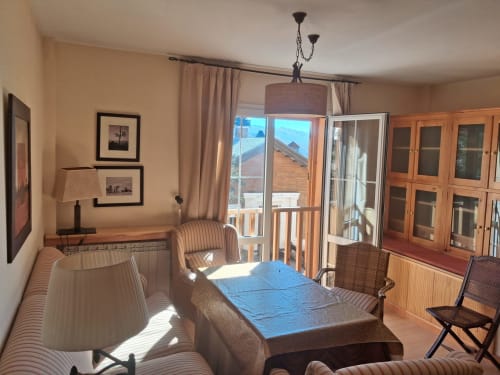 Luminosa sala de estar en cabaña de Sierra Nevada con vistas montañosas, muebles de madera, mesa azul y grandes puertas de cristal