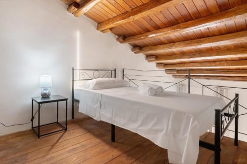 Rustic loft bedroom at Sikania Agri Relais with exposed wooden beams, metal bed frame, white linens, and mountain views from