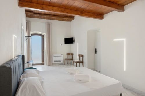 Bright modern triple room at Sikania Agri Relais in Caccamo with white bedding, wooden beams, mountain view, and contemporary