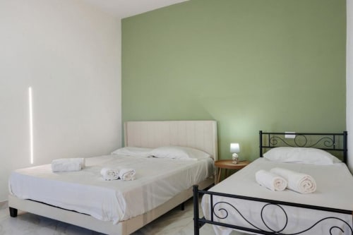 Two beds with white linens in Sikania Agri Relais apartment, Caccamo, with sage green accent wall and mountain views