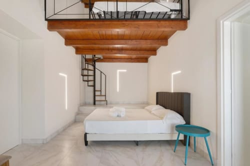 Modern bedroom at Sikania Agri Relais in Caccamo with exposed wooden beams, spiral staircase, white walls, and turquoise side