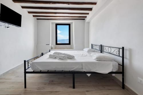 Bright bedroom at Sikania Agri Relais in Caccamo with black metal bed, white linens, mountain view window, and exposed wooden