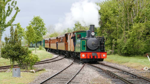 Train à vapeur historique au moteur rouge et voitures anciennes entourés d'arbres au château de Mons-Boubert