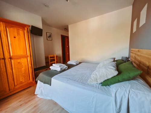 Bright double room at Balcó del Priorat hotel in Tarragona with wooden bed, white linens, green pillows, orange wardrobe, and