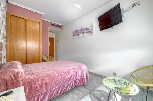Habitación doble en Hostal El Molino de Collado Villalba con cama rosa, armario de madera, TV y muebles modernos
