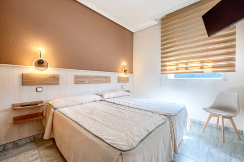 Moderno dormitorio doble en Hostal El Molino, Collado Villalba, con camas gemelas, iluminación cálida y ventana con vistas a la ciudad