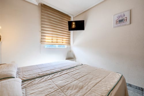 Habitación luminosa con dos camas en Hostal El Molino de Collado Villalba, con TV, persianas rayadas y vistas a la ciudad