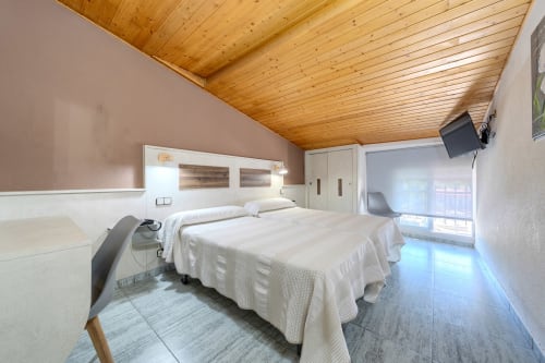 Dormitorio moderno en el desván del Hostal El Molino en Collado Villalba con dos camas, techo de madera y acceso a balcón