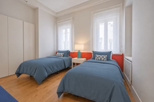 Dormitorio doble en Andimi Apartaments Madrid con ropa de cama azul, cabeceros rojos, suelo de madera y vistas a la ciudad