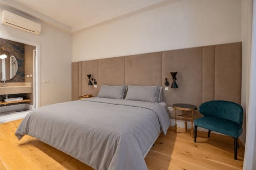 Dormitorio moderno en Andimi Apartments Madrid con cama gris, cabecero beige, suelos de madera y silla de acento azul verdoso