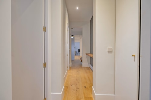 Pasillo moderno en apartamento madrileño con puertas blancas, suelo de madera e iluminación empotrada hacia la sala de estar