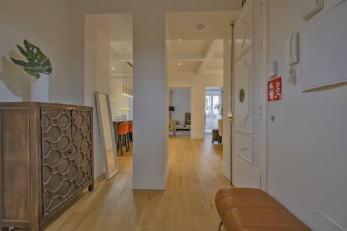 Pasillo de apartamento moderno en Madrid con suelos de madera, paredes blancas y mobiliario contemporáneo que conduce al salón