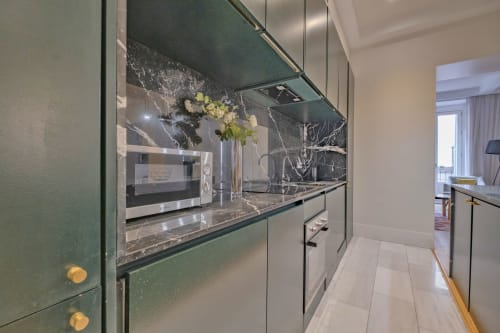 Cocina moderna en apartamento madrileño con muebles verdes, pared de mármol y electrodomésticos de acero inoxidable