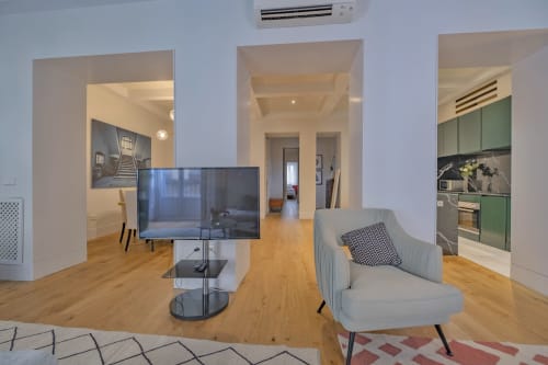 Salón moderno de apartamento en Madrid con TV, sillón gris, suelos de madera, cocina abierta y aire acondicionado