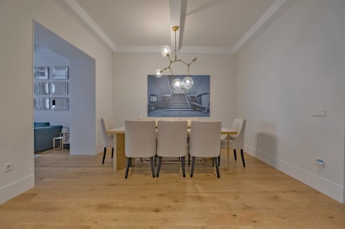 Comedor moderno en apartamento de Madrid con mesa de madera, sillas color crema, iluminación colgante y obras de arte con vistas a la ciudad