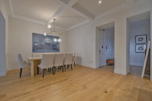 Comedor moderno en apartamento madrileño con mesa de madera, sillas color crema, iluminación colgante y techo artesanado