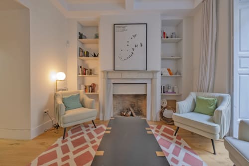 Elegante sala de estar de apartamento madrileño con chimenea, dos sillones, estanterías empotradas y alfombra con patrón geométrico