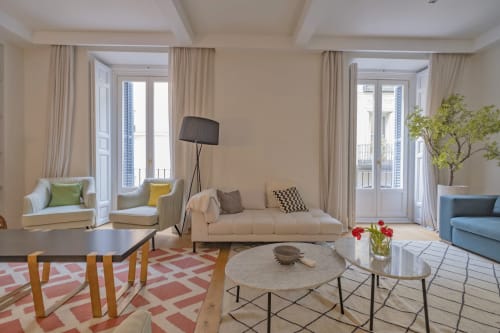 Elegante salón de apartamento madrileño con sofá crema, sillas coloridas, vistas a la ciudad y mobiliario moderno
