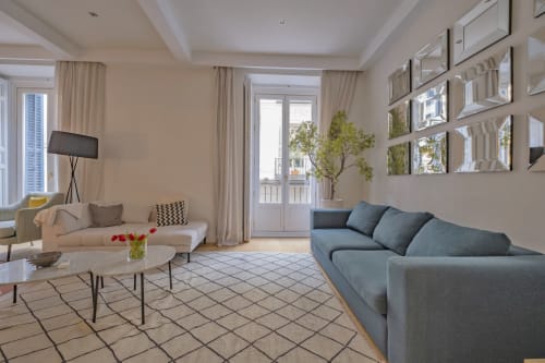 Sala moderna en Andimi Apartments Madrid con sofá azul, seccional beige, balcón con vistas a la ciudad y decoración contemporánea