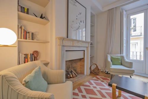 Sala de estar de apartamento moderno en Madrid con chimenea, estanterías empotradas, mobiliario crema y vistas a la ciudad desde el balcón