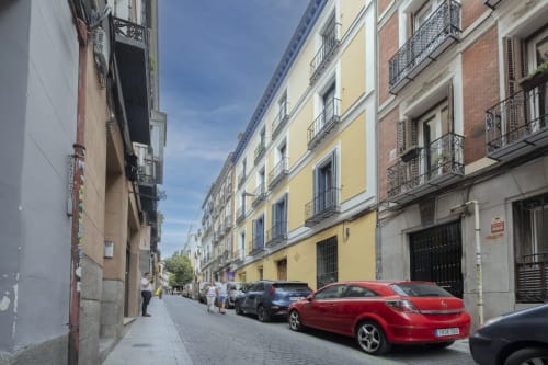 Vista de calle madrileña con edificios residenciales coloridos, autos estacionados y peatones cerca del hotel Andimi Apartaments