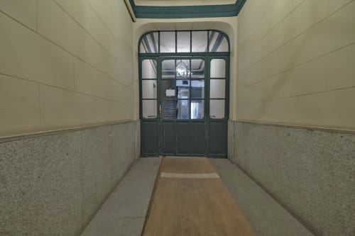 Entrada moderna de apartamento en Madrid con paredes de terrazo, puertas de cristal con marco oscuro y suelo de madera