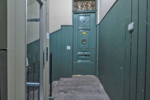 Estrecho pasillo de apartamento madrileño con paredes de paneles verdes y elegante puerta de entrada en color azul teal