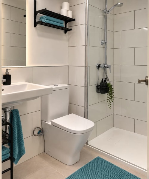 Modernes Badezimmer mit weißen U-Bahn-Fliesen, weiße Toilette, begehbare Dusche mit Regenschauer, schwarze Regale, türkise Handtücher