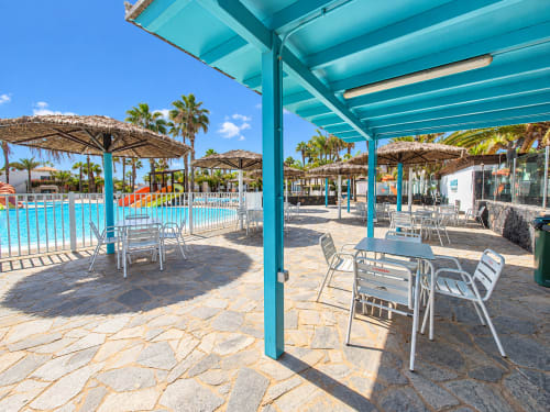 Türkisfarbene Poolterrasse mit Esstischen, Sonnenschirmen und Palmen im Sara & Gino Fuerteventura in Corralejo