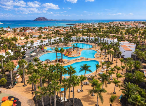 Luftaufnahme des Sara & Gino Fuerteventura Resorts in Corralejo mit Pools, Palmen und türkisblauem Meer
